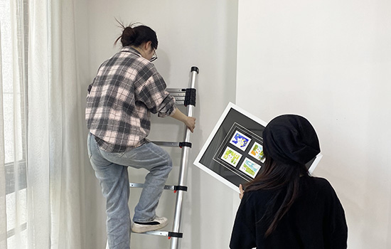 Duas meninas estão usando uma en131 escada telescópica para pendurar uma pintura