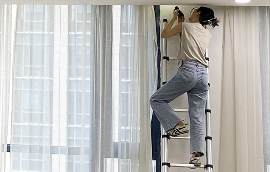Uma garota está subindo uma en131 escada telescópica para consertar cortinas